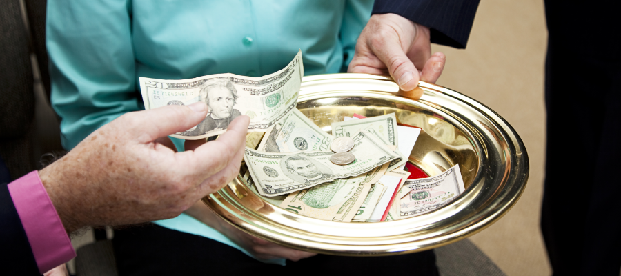 person putting a twenty dollar bill in a gold collection plate.