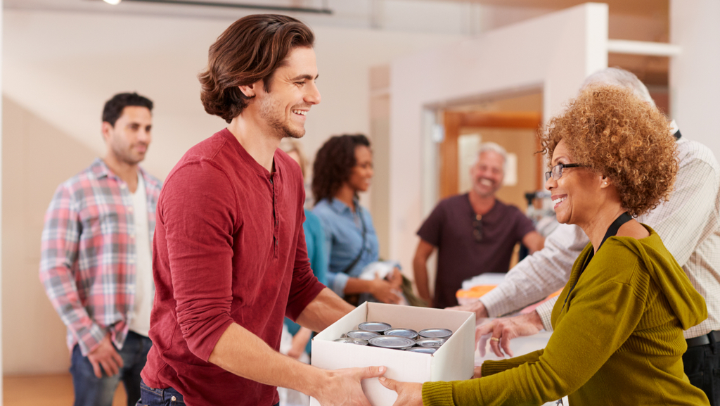 A smiling man and woman happily exchanging a box of goods for a canned food drive. 