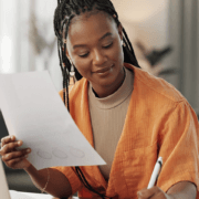 A woman in front of a computer holding a piece of paper and writing something down