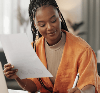 A woman in front of a computer holding a piece of paper and writing something down