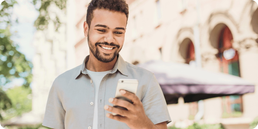man standing outside smiling while looking at his phone