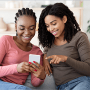 Two young Gen Z girls smiling while looking at a mobile phone
