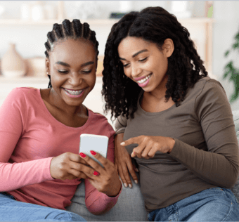 Two young Gen Z girls smiling while looking at a mobile phone