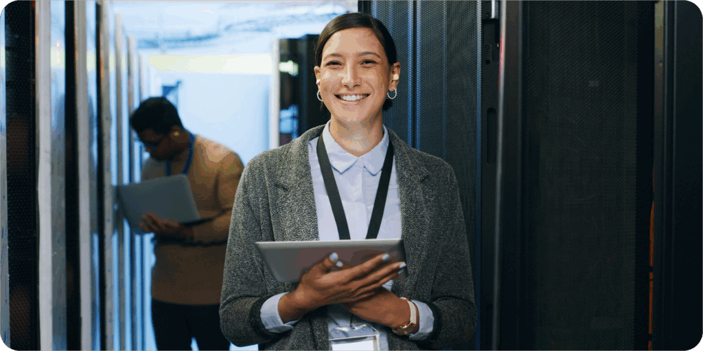 A woman smiling holding a tablet in a server room