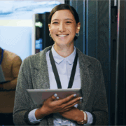 A woman smiling holding a tablet in a server room