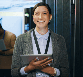 A woman smiling holding a tablet in a server room