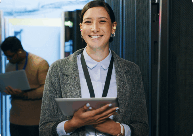 A woman smiling holding a tablet in a server room